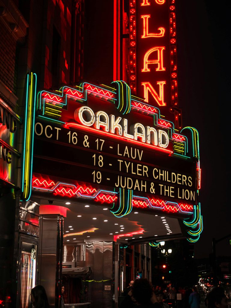 Illuminated neon sign at Oakland theatre showcasing upcoming concerts at night.